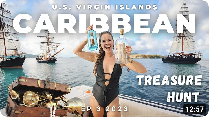 A woman in a black bathing suit poses on a ship with two liquor bottles with messages inside. There is a treasure chest with treasure beside her and sailboats on the water behind her.